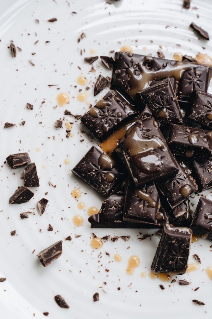 pexels-photo-4113352 Close-up of gourmet dark chocolate pieces drizzled with caramel on a white plate.